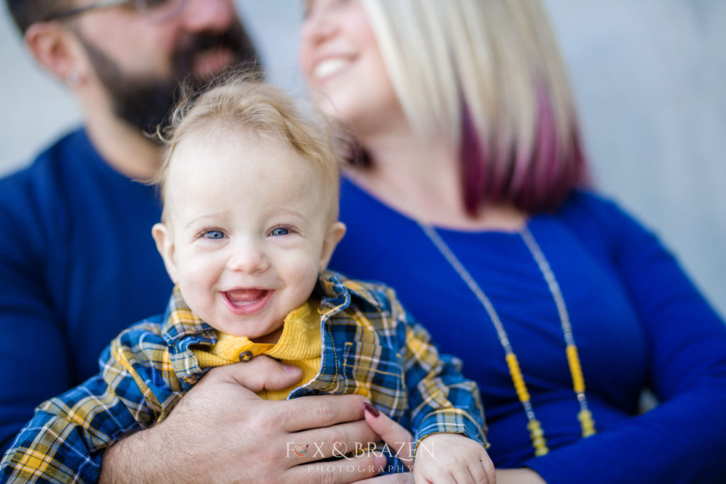 Little boy giggles while being held by his parents during a photography session in Phoenixville