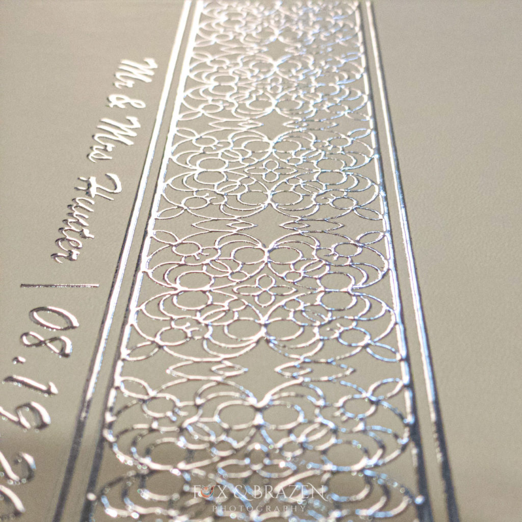 Raised silver foil on cover of wedding album in the pattern from their wedding invitation