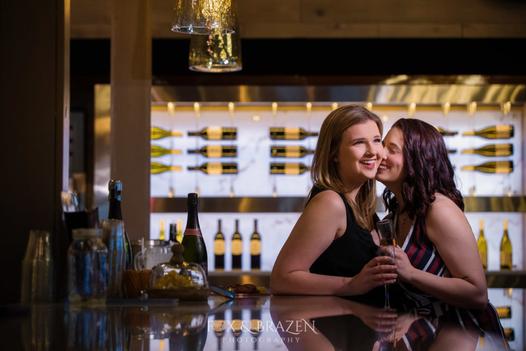 two adults standing a wine bar during engagement session