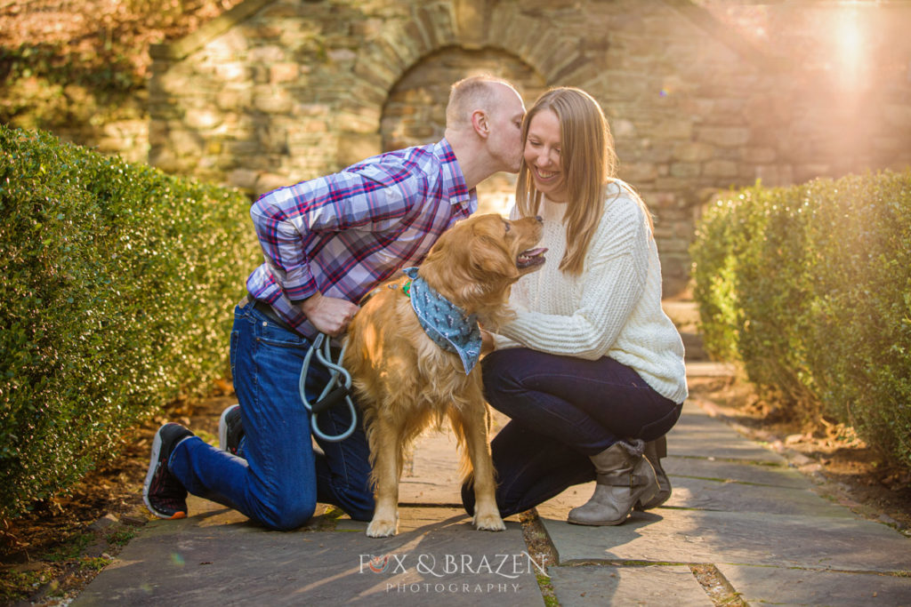 Young couple kissing with their dog at engagement session