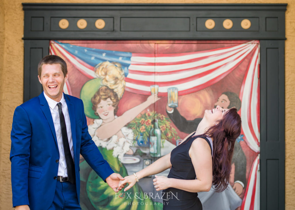 Two well dressed adults laugh in front of mural