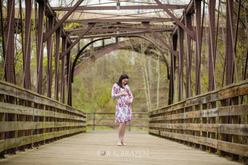 pregnant woman stands on bridge admiring belly