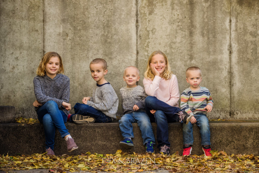 Five kids sitting against concrete wall