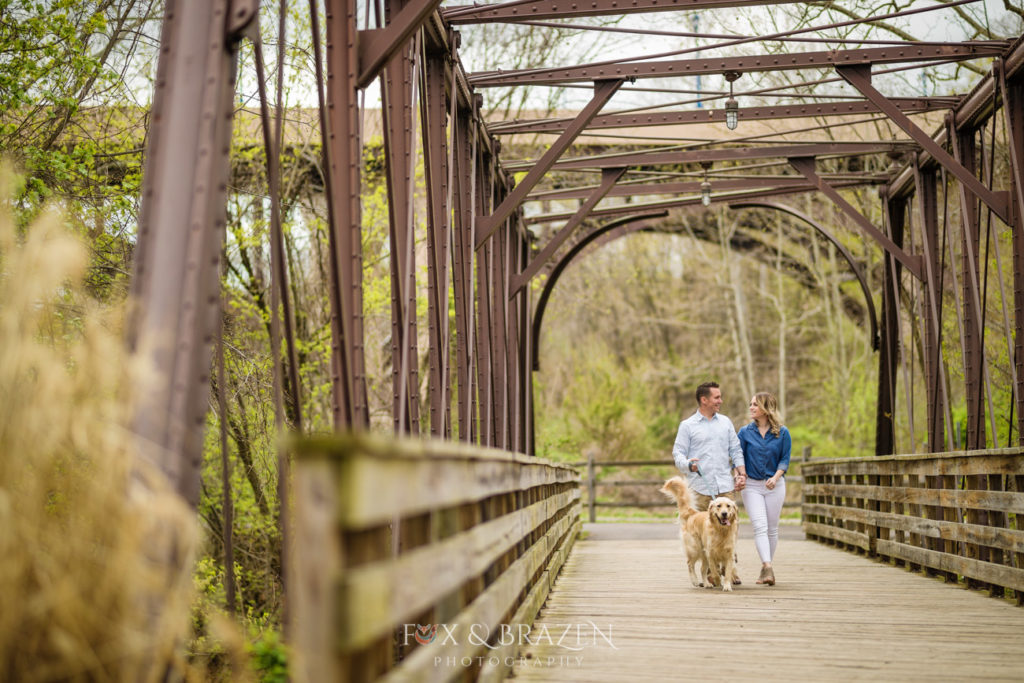 Young couple walks their golden retriever dog on bridge