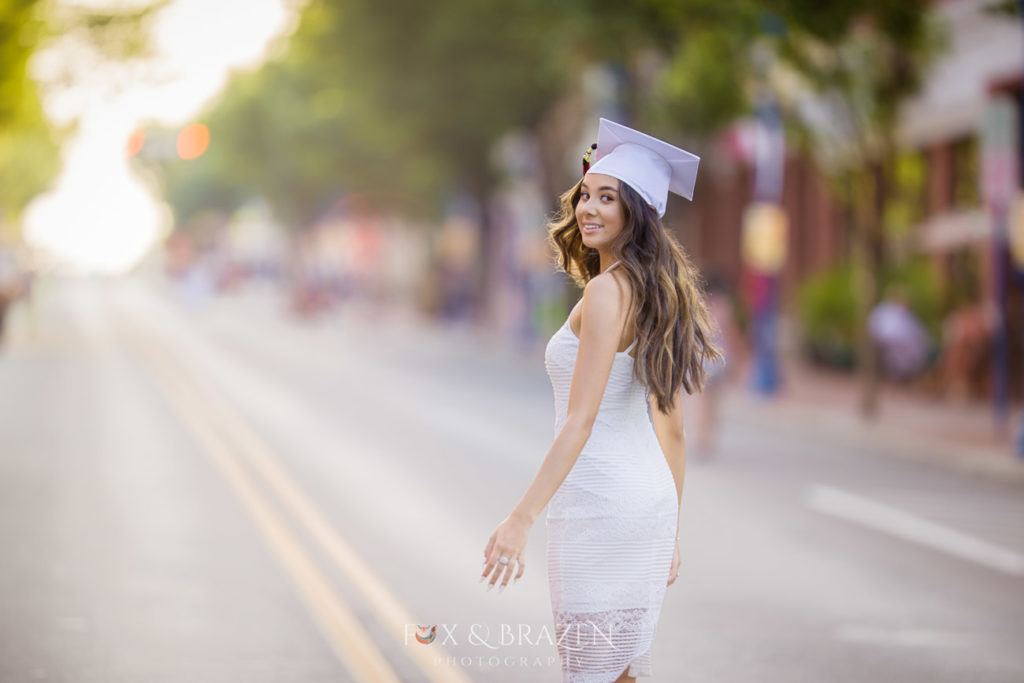 Girl in cap and gown walks down the middle of a street