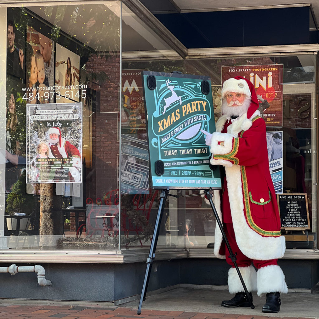 Santa stands next to a poster advertising a Christmas Party today.