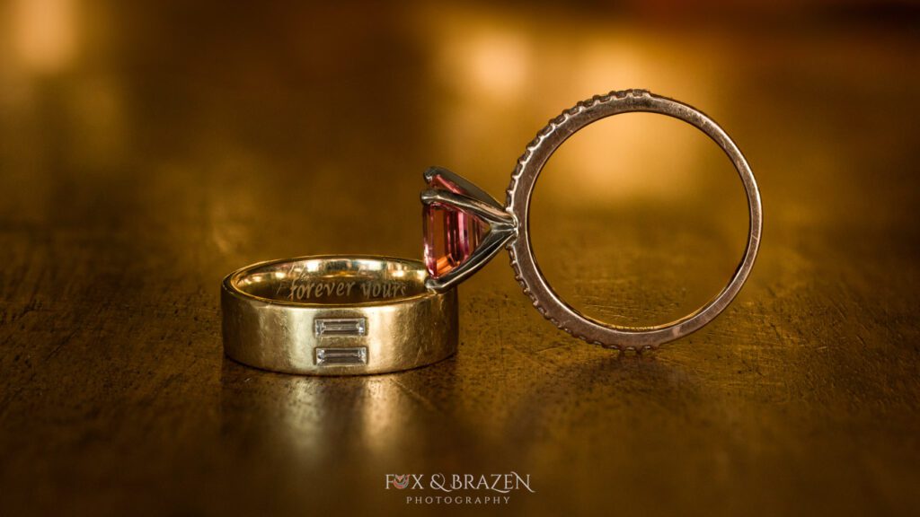 Macro photo of two engagement rings resting together, one with a pink stone and one engraved gold band.