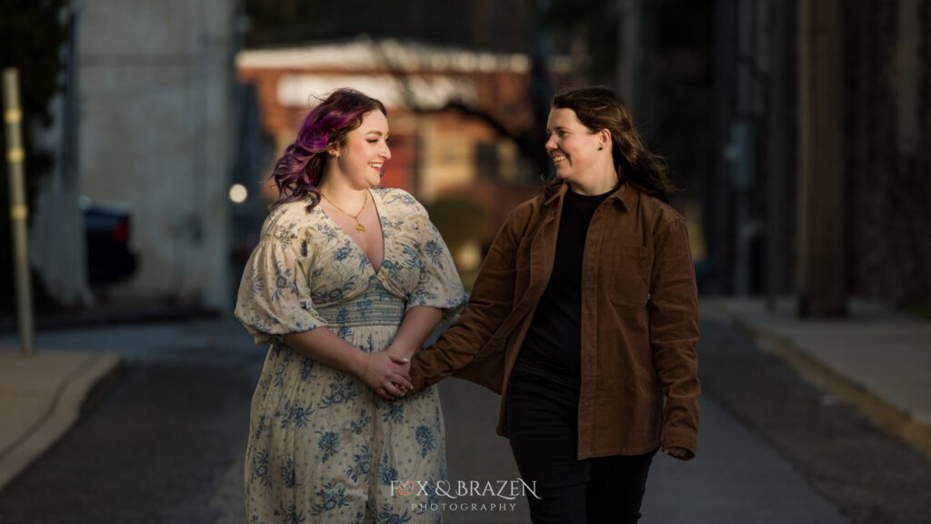 Engaged couple walking hand-in-hand through a sunlit alley for their Downtown Phoenixville engagement adventure