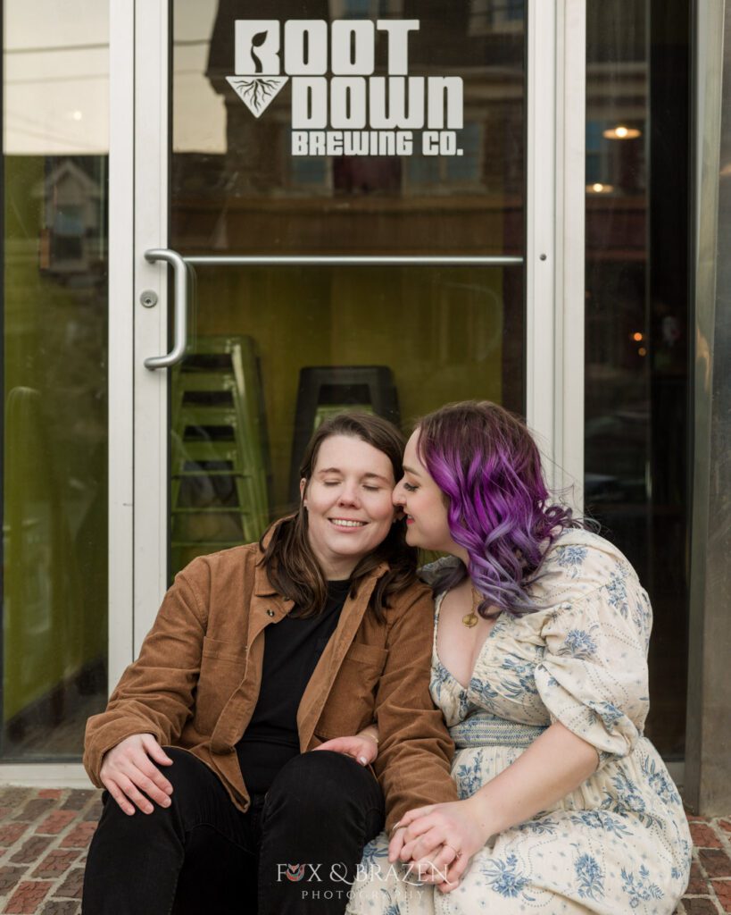 Engaged couple sits outside Root Down Brewing Co with eyes closed in a moment together.