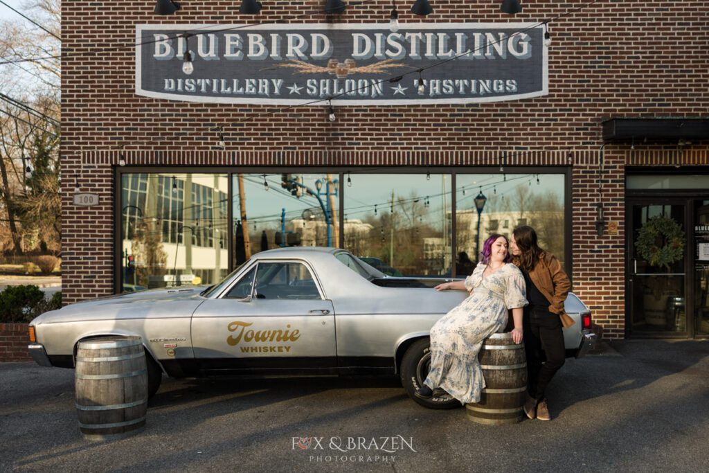 Engaged couple posing with the El Camino outside Bluebird Distilling for their Downtown Phoenixville engagement adventure.