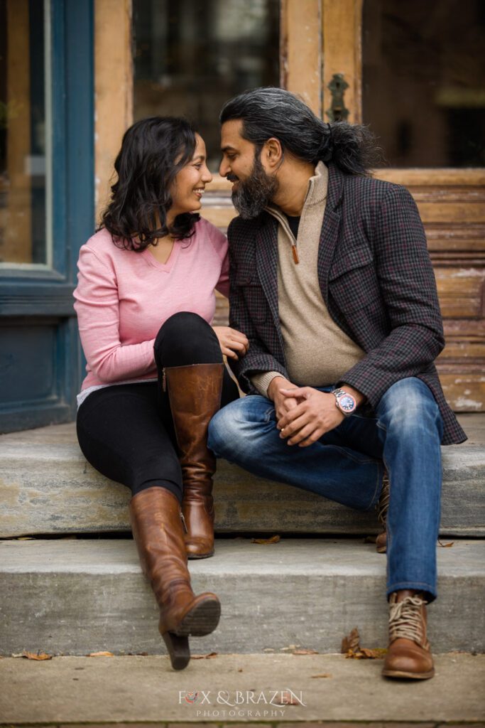 Engaged couple sitting on stone steps in Phoenixville near a wooden door