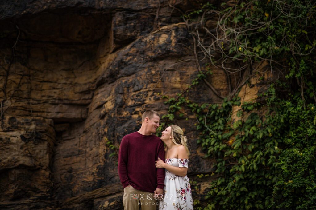 Couple snuggling by rock wall in Phoenixville