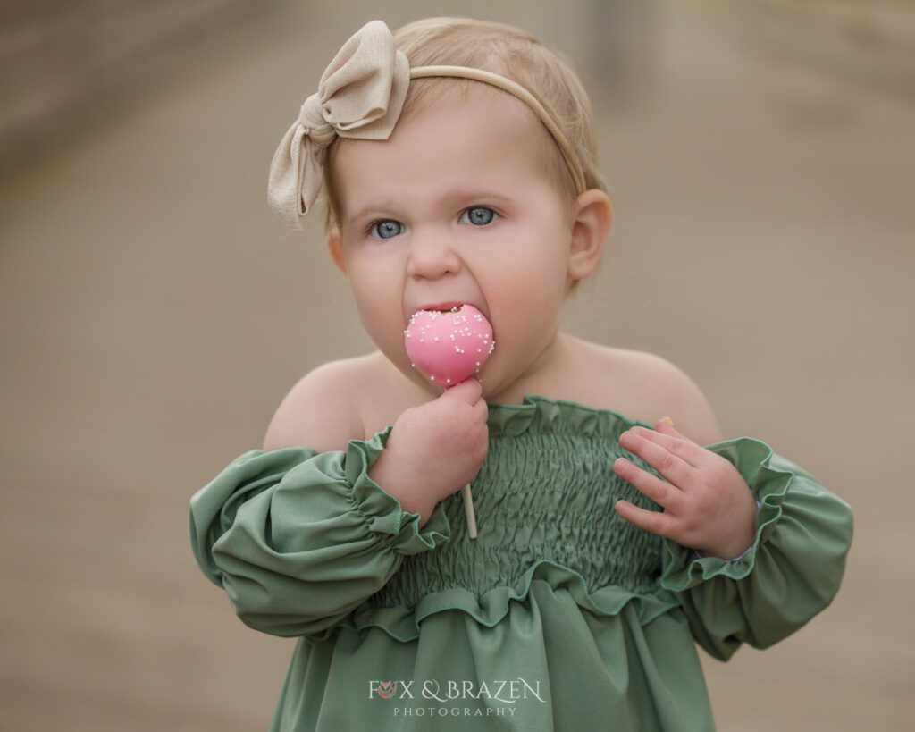Little girl in green dress enjoying a cake pop outdoors during summer vibes lifestyle session
