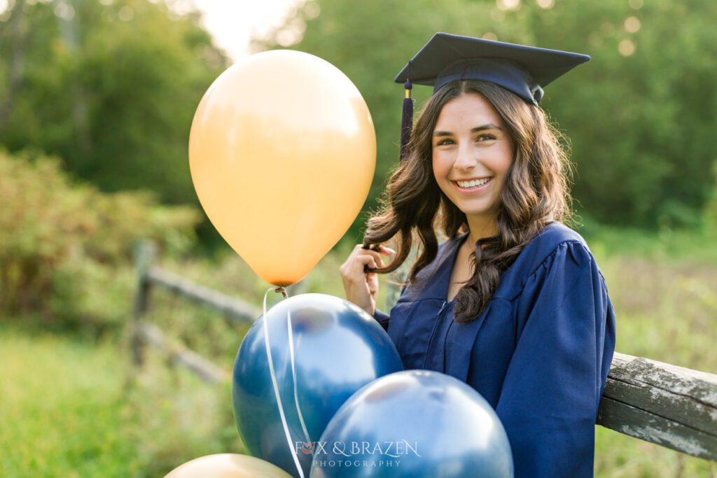 Senior girl in blue cap and gown holding balloons for 2025 high school graduation photos summer vibes lifestyle session