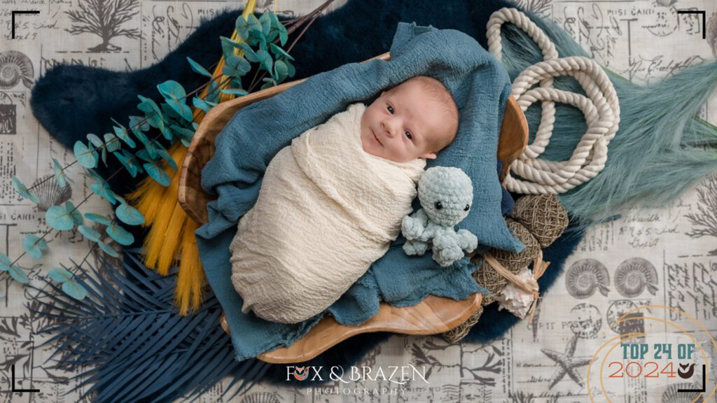 Awake newborn on an ocean-themed photography set with an octopus toy.