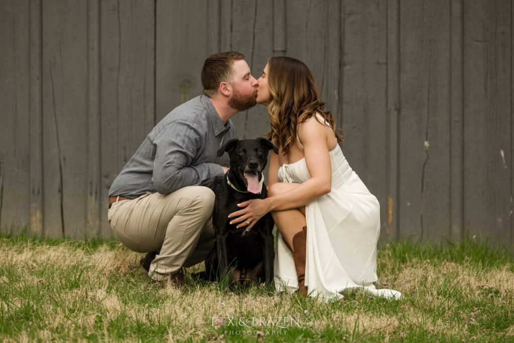 Couple kissing over their dog during engagement photos.