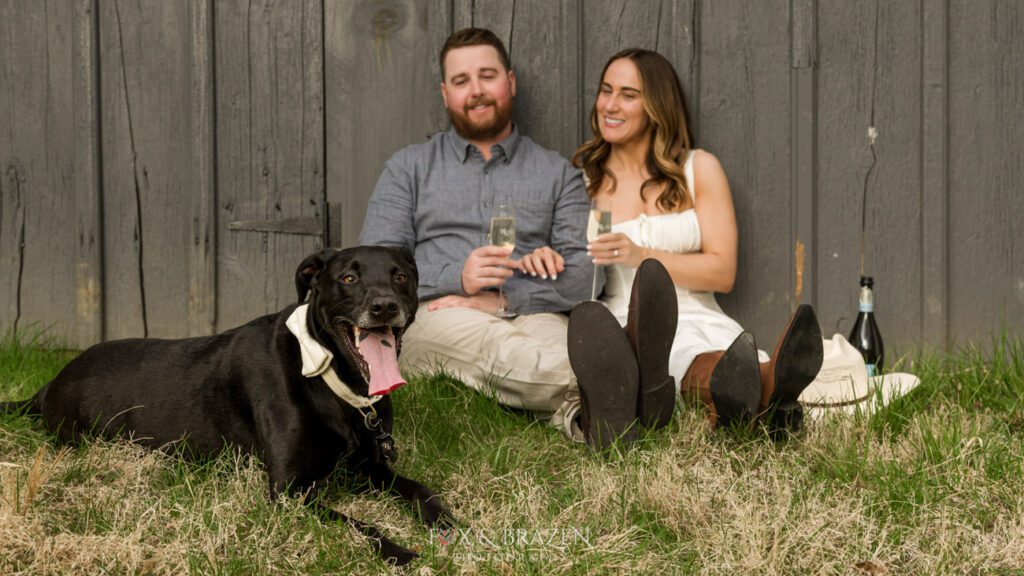 Dog in a bowtie sitting with a couple during engagement photos.