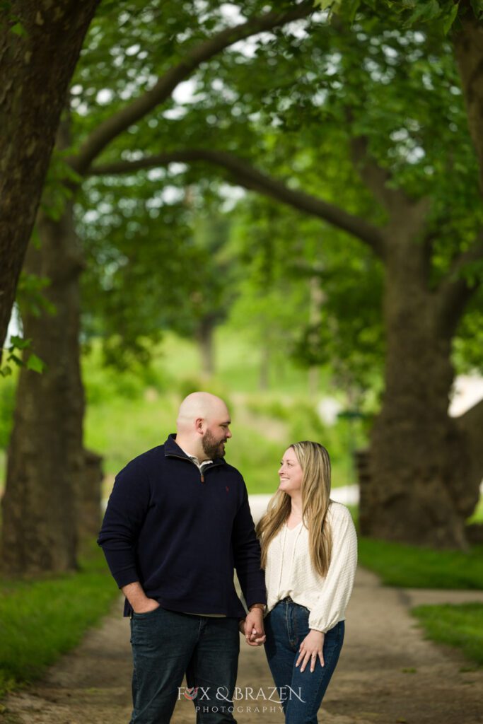 Engaged couple standing on a pathway at Valley Forge, gazing into each other’s eyes.