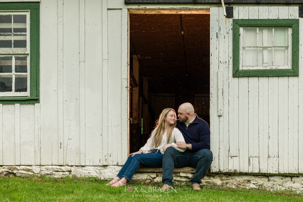 Engaged couple sitting in a rustic barn, sharing a tender moment during their Valley Forge session.