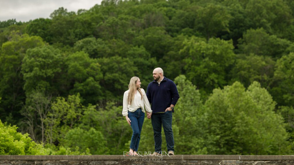 Couple standing on a stone wall, gazing at each other lovingly during their Valley Forge session.