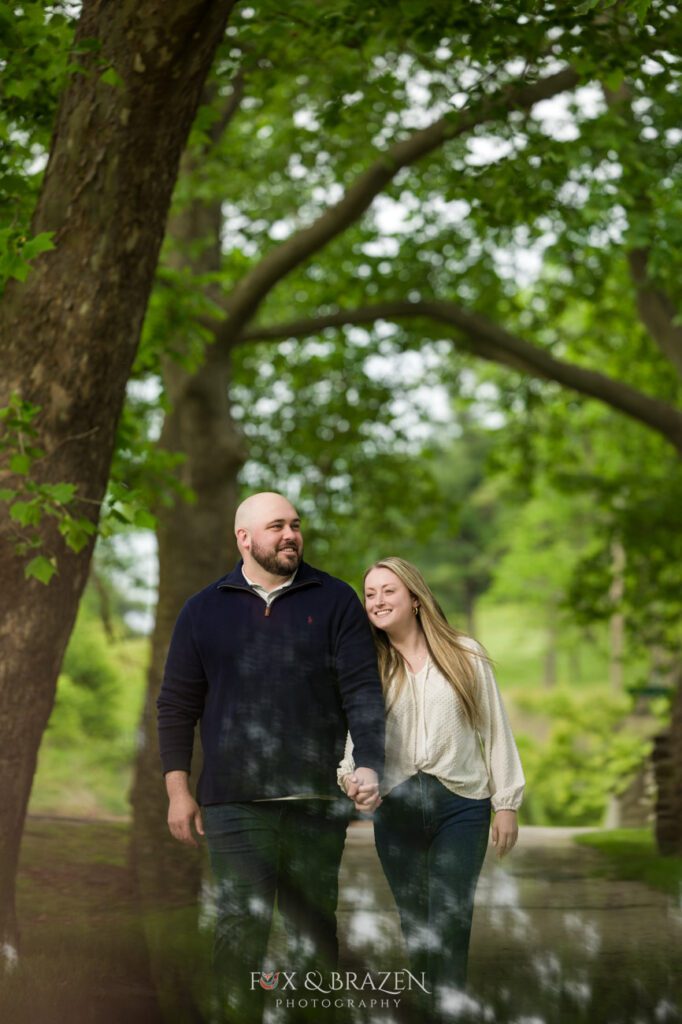 Engaged couple walking hand-in-hand with a dramatic lighting flare at Valley Forge.