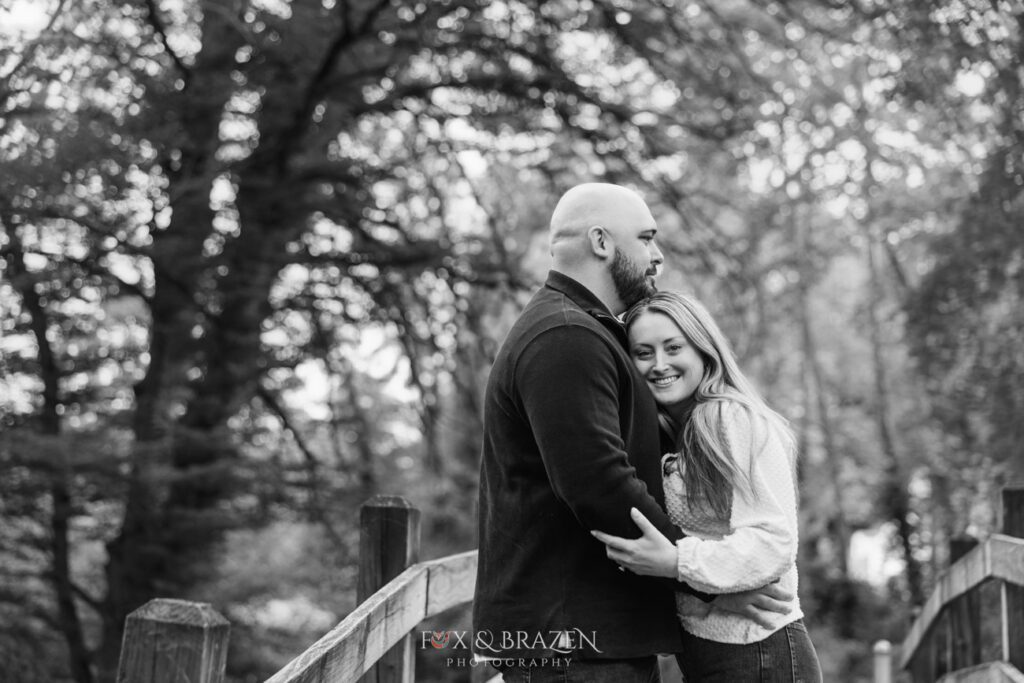 Black and white image of woman looking at the camera while being embraced by her fiancé at Valley Forge.