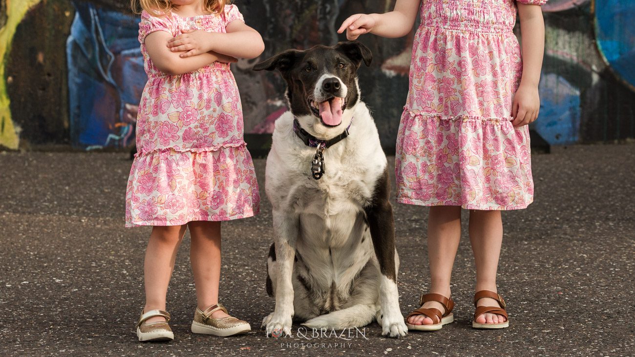 Dog posing in front of Phoenixville mural with two girls with faces hidden because privacy matters.