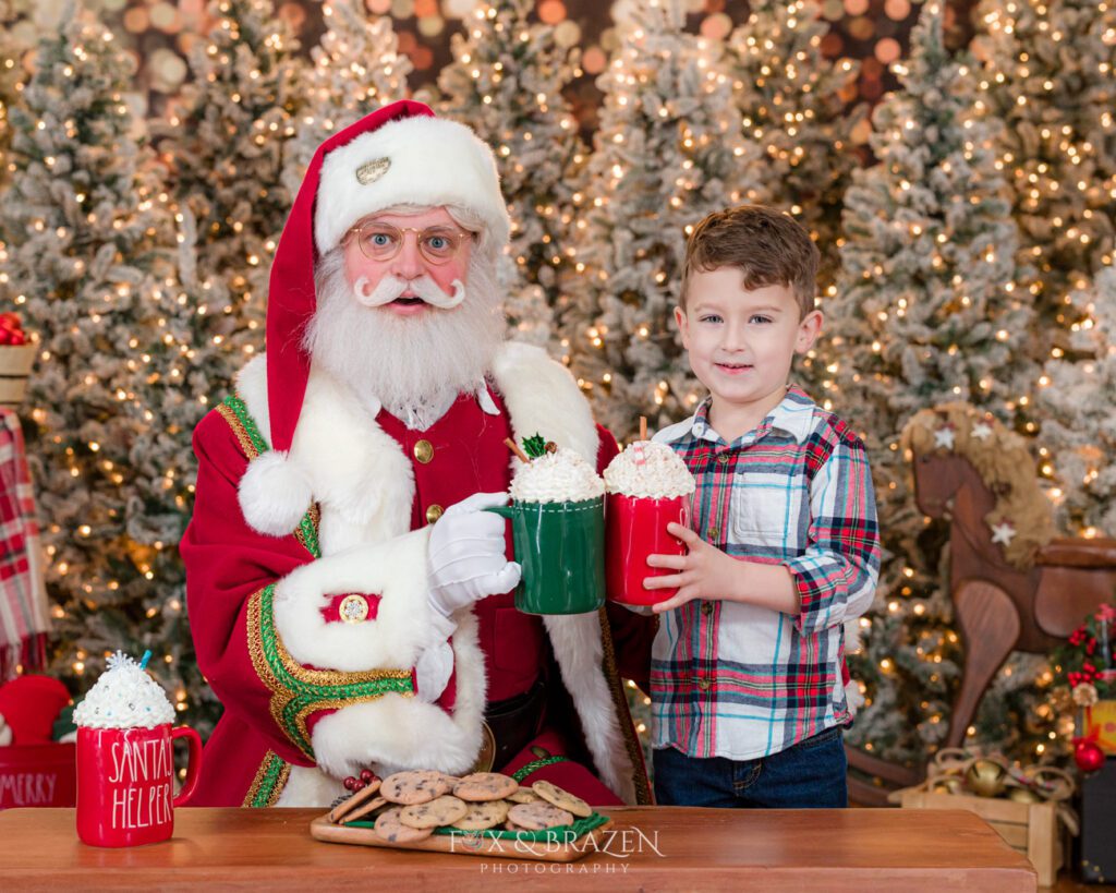 Santa Claus sharing hot cocoa and cookies with a little boy in a plaid shirt